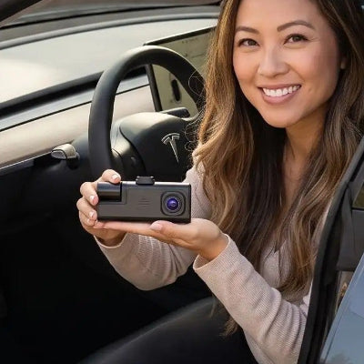 Femme contente  assise au volant présente dans sa main une camera pour voiture Double objectif Avant